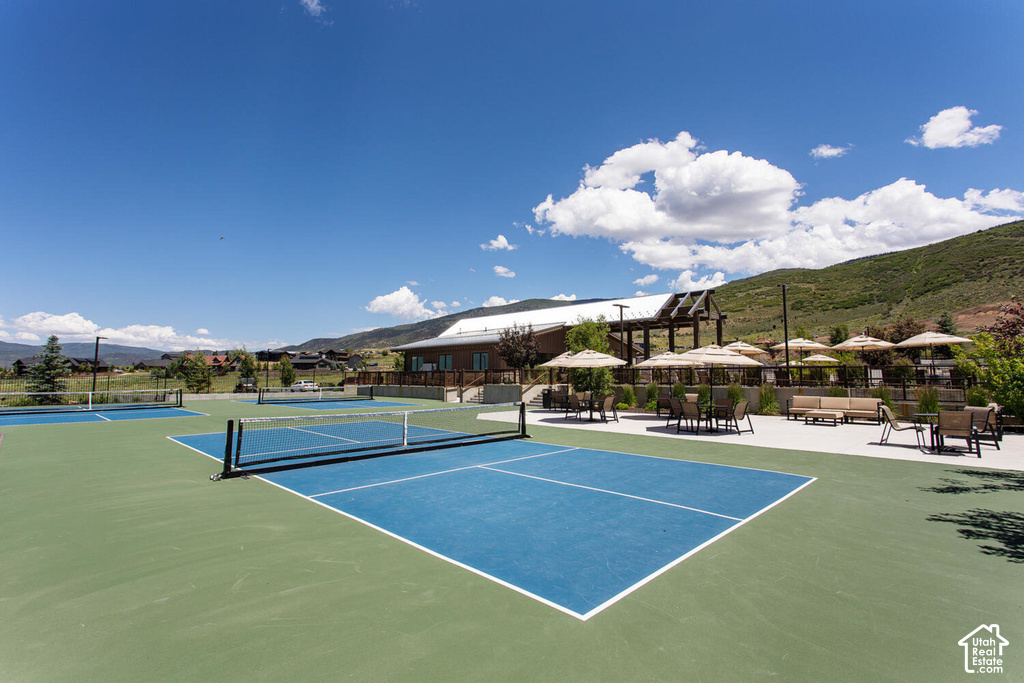 Multiple hard tennis courts, mountain backdrop, permanent building structure, outdoor seating areas, and a covered pergola