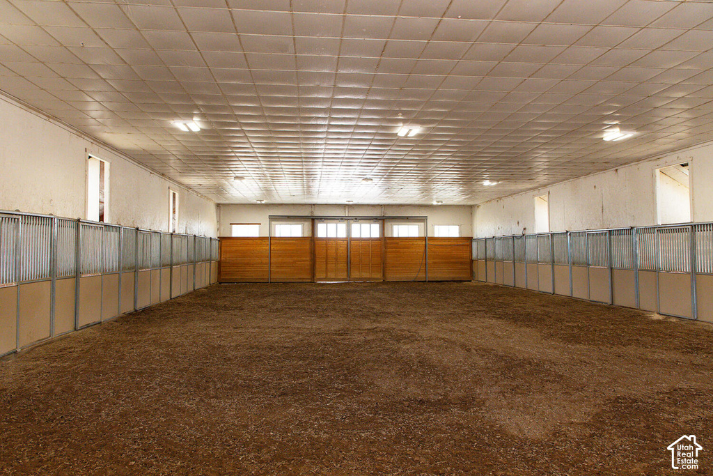 Indoor arena with an earth floor, perimeter stalls featuring metal grates, and wood-paneled walls