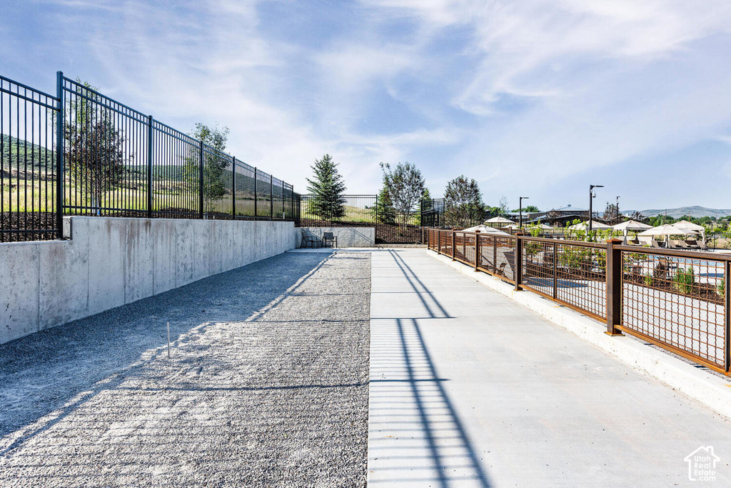 Concrete walkway and gravel area bordered by a black metal fence and a weathered metal railing with grid infill