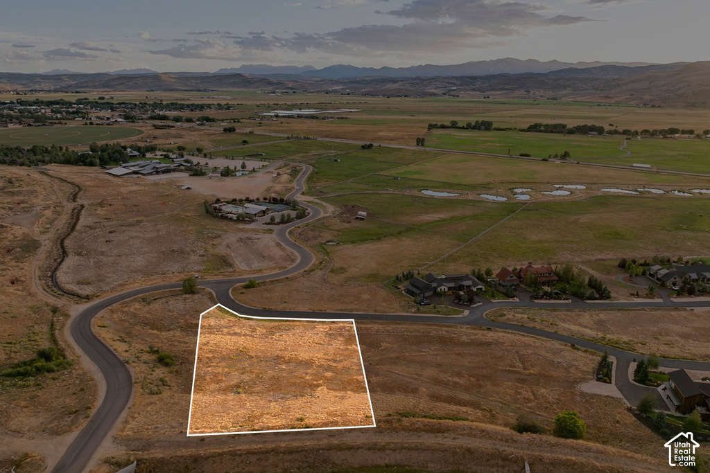 Expansive undeveloped land parcel with surrounding paved roads, distant residential structures, and natural terrain