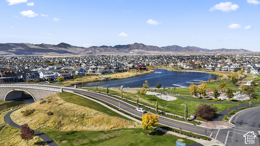 Expansive community featuring numerous residential properties, a large central lake, manicured green spaces, paved pathways, and a stone arch bridge