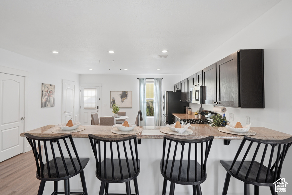 Kitchen featuring an eat-at island with a stone-finish countertop, black cabinetry, recessed lighting, and wood-finish flooring
