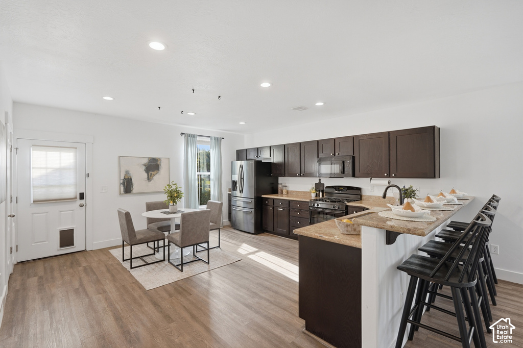 Open-concept kitchen featuring dark wood cabinetry, light-colored countertops, stainless steel appliances, and wood-finish flooring