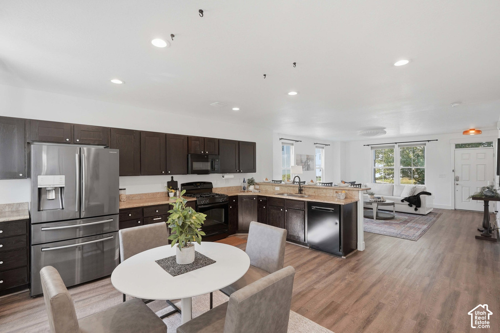 Open-concept living space with wood-finish flooring, recessed lighting, and a kitchen featuring dark cabinetry, stainless steel appliances, and light-toned countertops