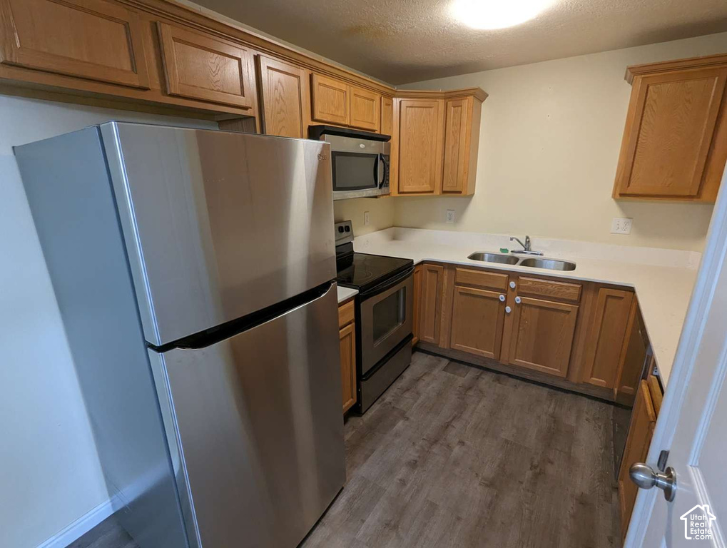 Kitchen featuring wood-finish cabinetry, stainless steel appliances, a double basin sink, light-toned countertops, and wood-finish flooring