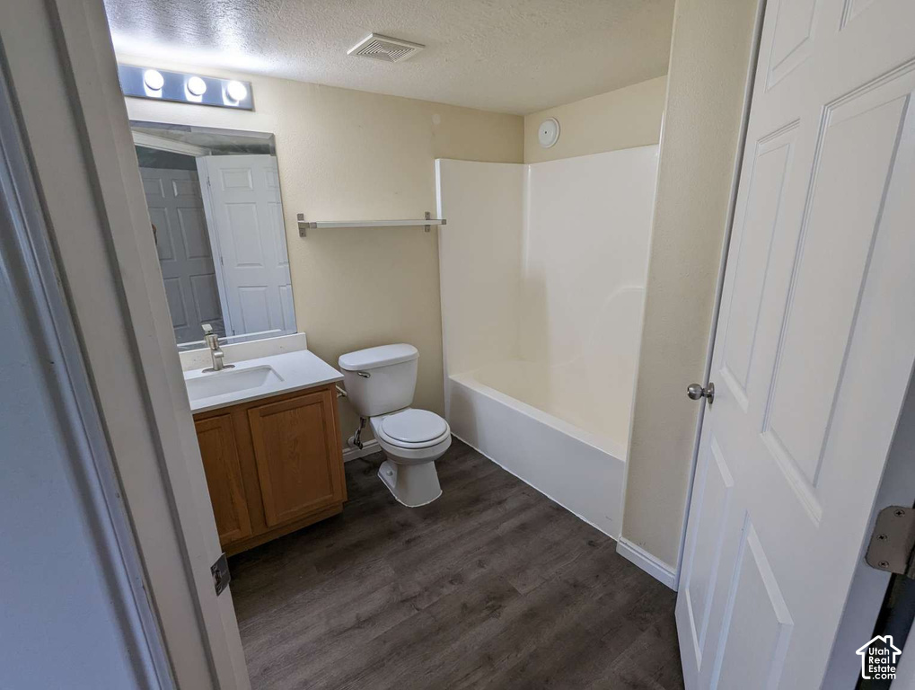 Bathroom featuring wood-finish flooring, a single vanity with an integrated sink, a toilet, and a combined tub and shower unit
