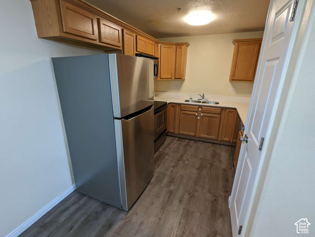 Stainless steel refrigerator, built-in cabinetry, wood-finish flooring, stainless steel sink, and light-toned countertops
