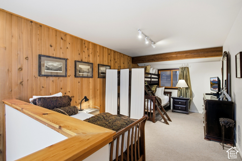 Vertical wood-paneled accent wall, exposed wood beam ceiling, track lighting, and carpeted flooring