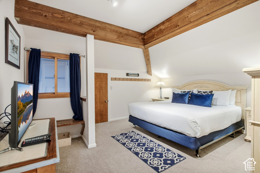 Vaulted ceilings with exposed wood beams, neutral-toned carpeting, wood-finish window frames, and wood-finish door