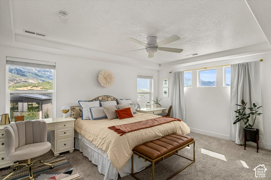 Recessed ceiling with a modern ceiling fan, large windows with scenic mountain backdrop, and light-colored carpeting
