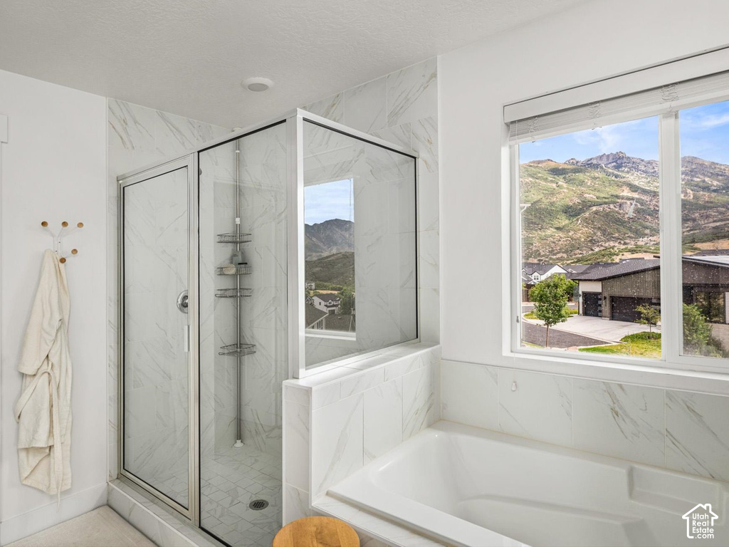 Spacious bathroom featuring a built-in tub, a glass-enclosed shower with tiled walls, and a large window