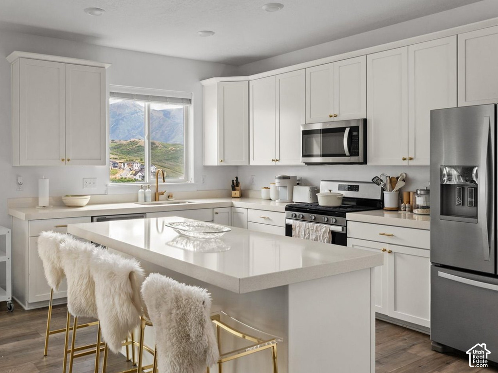 Contemporary kitchen featuring white cabinetry, stainless steel appliances, a center island with countertop seating, and wood-finish flooring