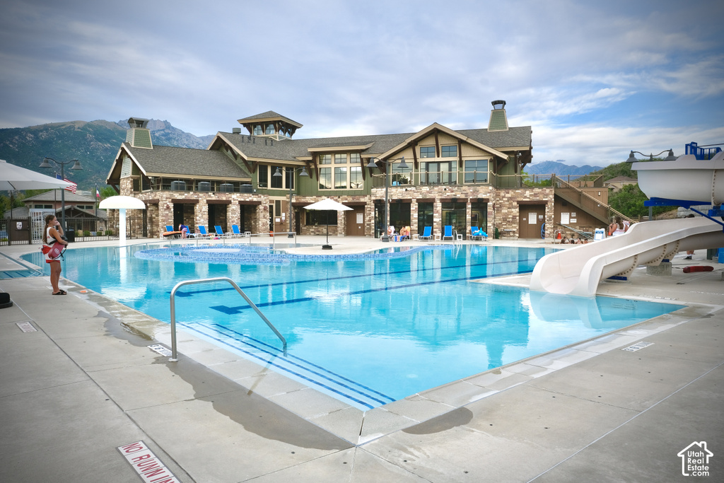 Expansive outdoor pool with a water slide, integrated sun shelf, and adjacent multi-story clubhouse featuring stone and wood siding