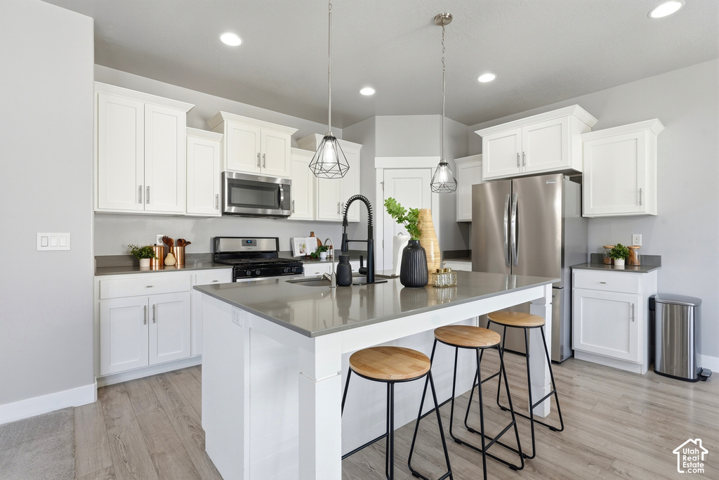 Kitchen featuring white cabinetry, stainless steel appliances, a center island with countertop seating, wood-finish flooring, and recessed lighting