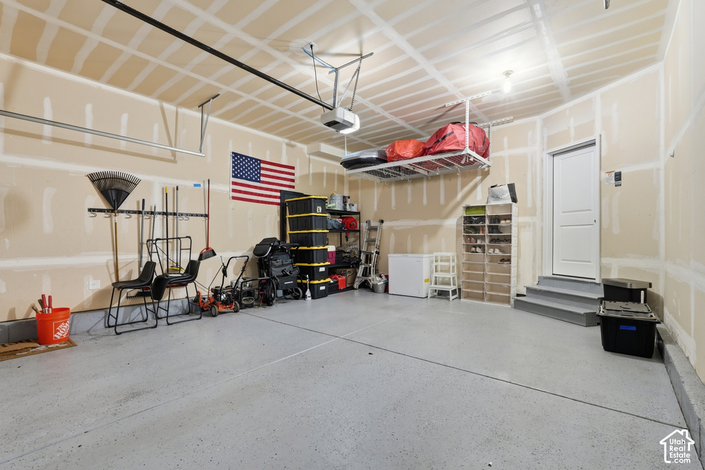 Garage featuring a gray epoxy floor coating, exposed ceiling joists, and a white entry door with gray steps