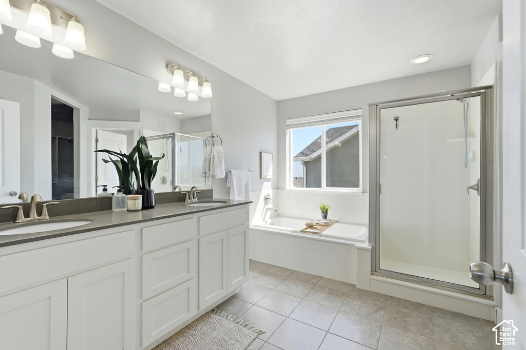 Dual vanity with undermount sinks, full-width mirror, tile flooring, glass-enclosed shower, and built-in tub with window