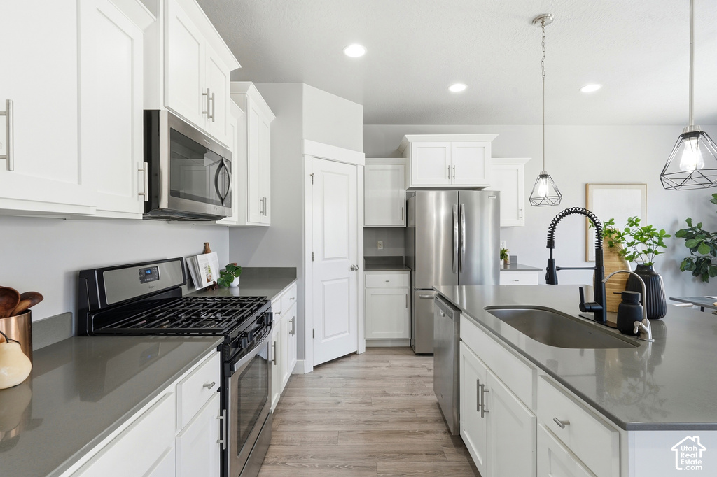 Kitchen featuring white shaker cabinetry, stainless steel appliances, dark countertops, and wood-finish flooring