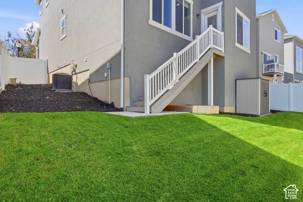 Landscaped yard featuring a white vinyl fence, exterior stairs with white railings, and a storage shed