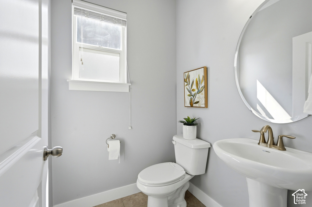 Pedestal sink with a brass-finish faucet, circular wall mirror, and a single window