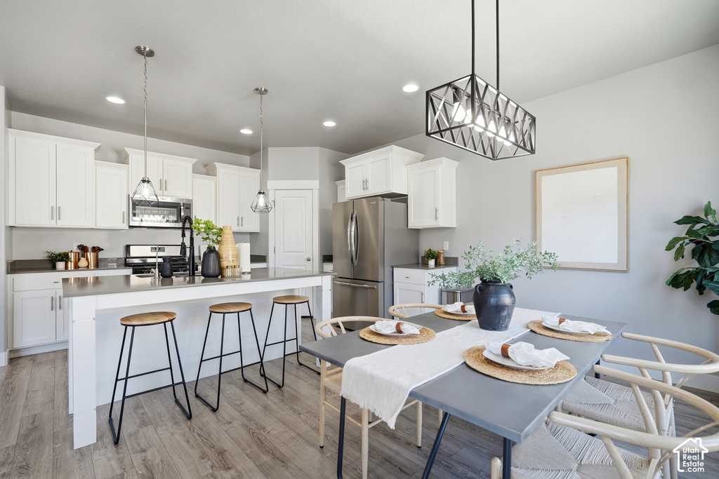 Open-concept kitchen and dining area featuring white cabinetry, stainless steel appliances, wood-finish flooring, and recessed lighting