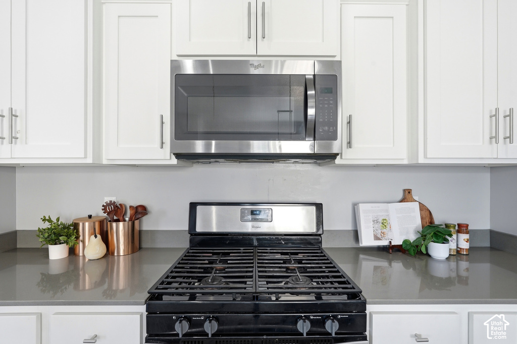 Stainless steel microwave, white shaker-style cabinetry with silver hardware, smooth grey countertops, and a black gas range