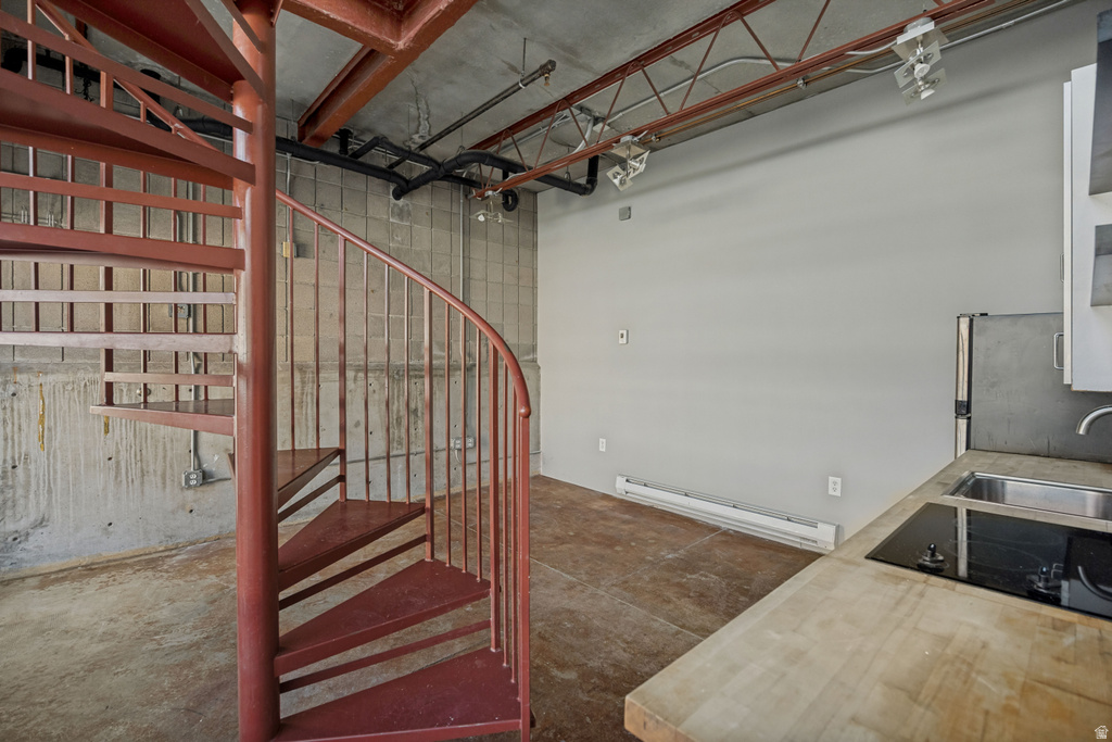 Red metal spiral staircase, concrete flooring, exposed ceiling beams, built-in cooktop, and stainless steel sink