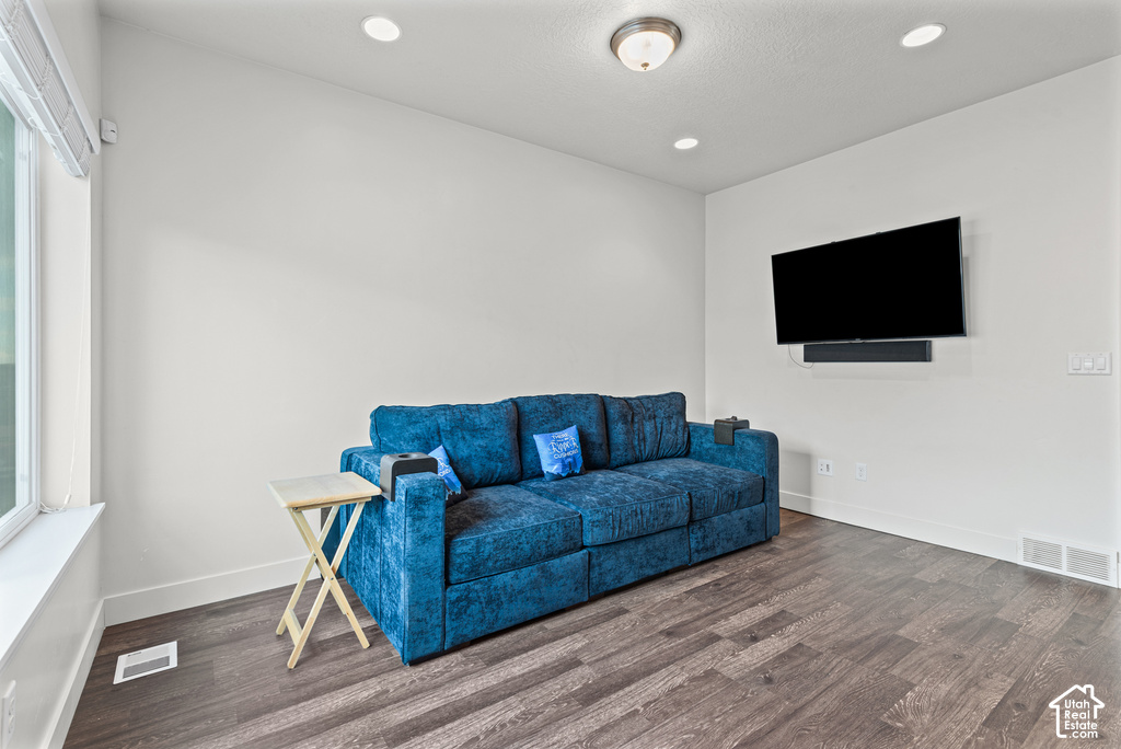 Modern recreation room featuring a wall-mounted flat-screen television, recessed ceiling lighting, large window with natural light, and wood-finish flooring throughout the space