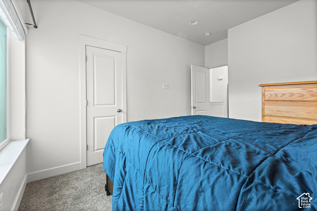Bright bedroom featuring neutral walls, recessed ceiling lighting, wood-finish dresser, carpeted flooring, and multiple closet doors for ample storage
