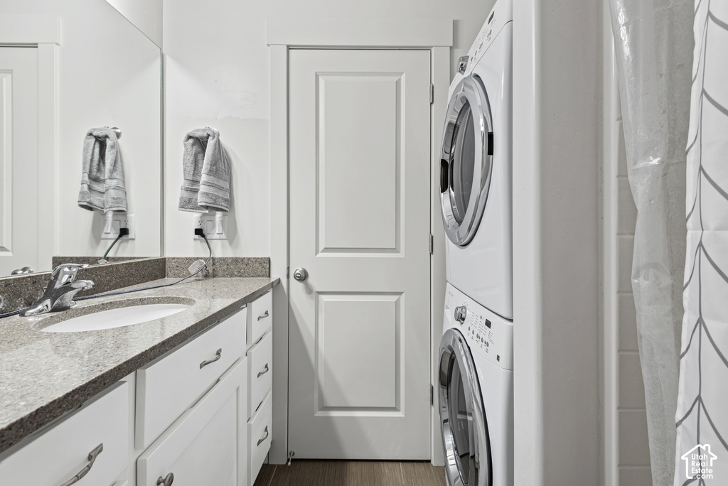 Modern utility room featuring dual front-load washers and dryers with stacked configuration, granite-topped vanity with dual vessel sinks and chrome fixtures, white cabinetry with brushed nickel hardware, and light wood-finish flooring throughout