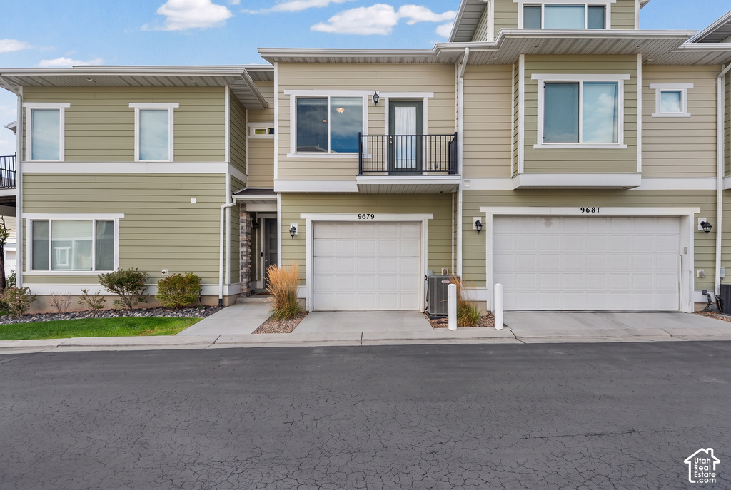 Modern townhome-style residences featuring clean-lined architectural design, composite siding exterior, attached two-car garages with white panel doors, second-story balconies with metal railings, and manicured front landscaping with seasonal plantings al