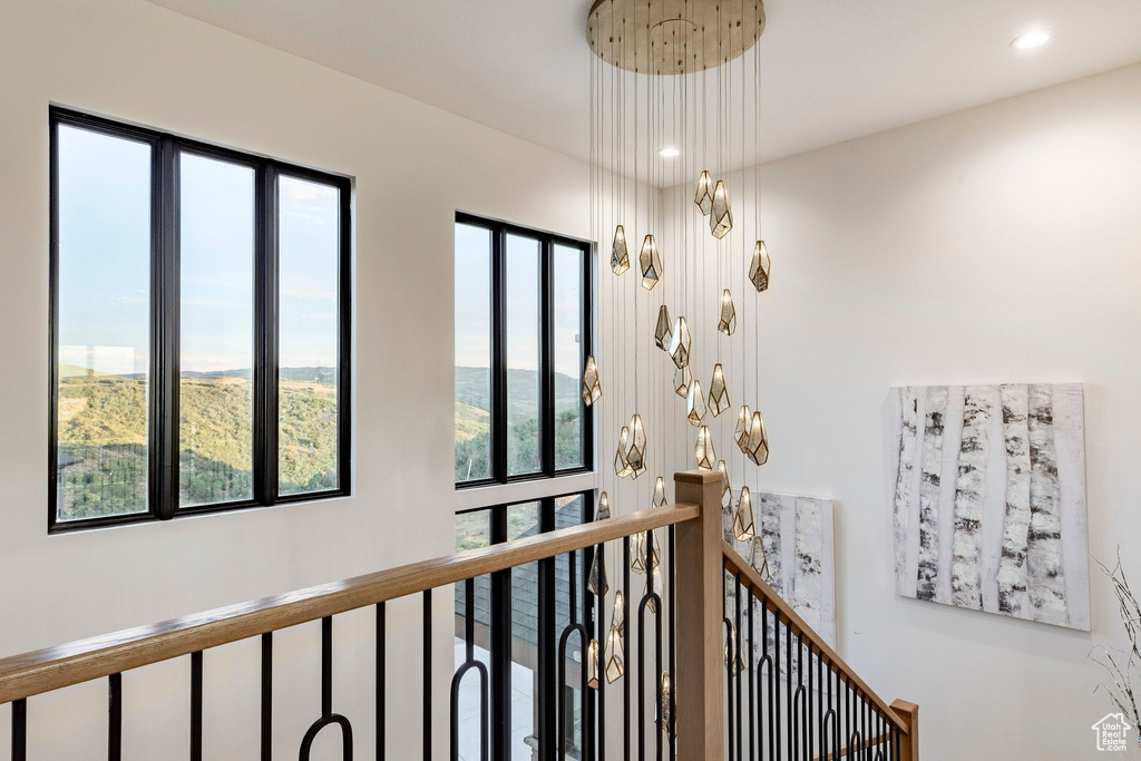 Modern multi-tier chandelier, black-framed windows, light wood handrail, and wrought iron balusters