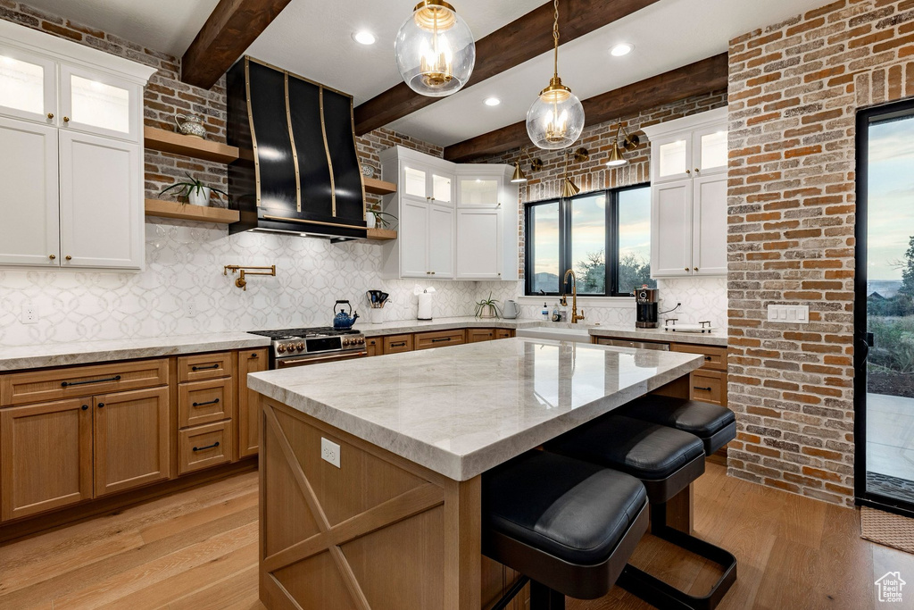 Gourmet kitchen featuring a large central island, exposed beam ceiling, brick accent wall, wood-finish flooring, and a patterned tile backsplash