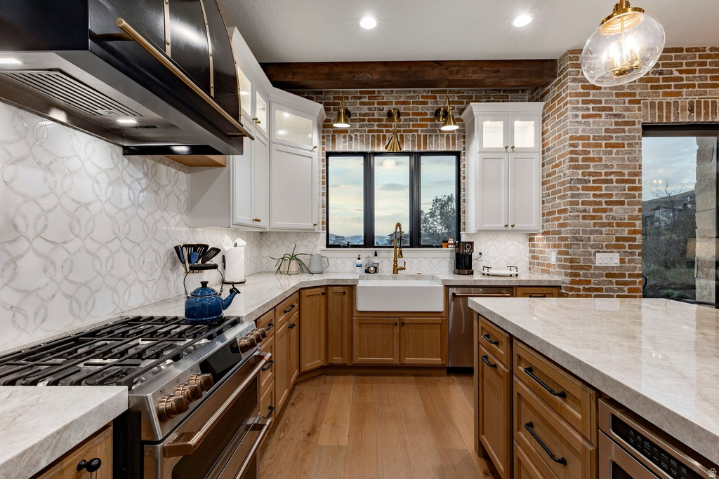 Gourmet kitchen featuring a built-in gas range, white shaker cabinetry, wood-finish lower cabinetry, light-toned countertops, and an exposed brick accent wall