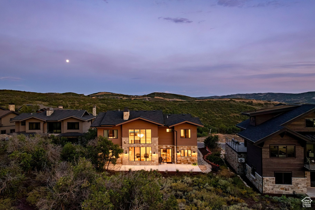 Multi-level property featuring extensive stone and wood siding, a dark shingle roof, and multiple large windows
