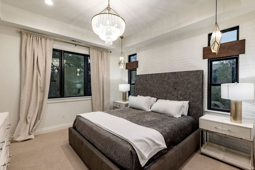 Recessed ceiling lighting, a prominent chandelier, textured brick wall accent, multiple windows, and low-pile carpeting