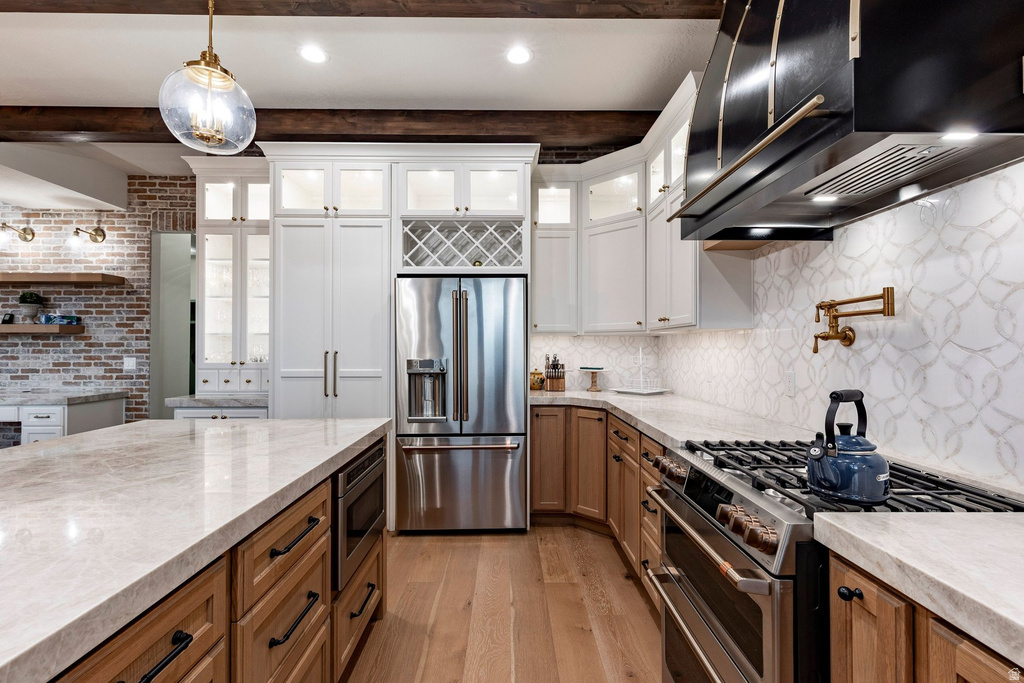 Kitchen featuring wood-finish flooring, stone countertops, stainless steel appliances, a pot filler, and a decorative tile backsplash
