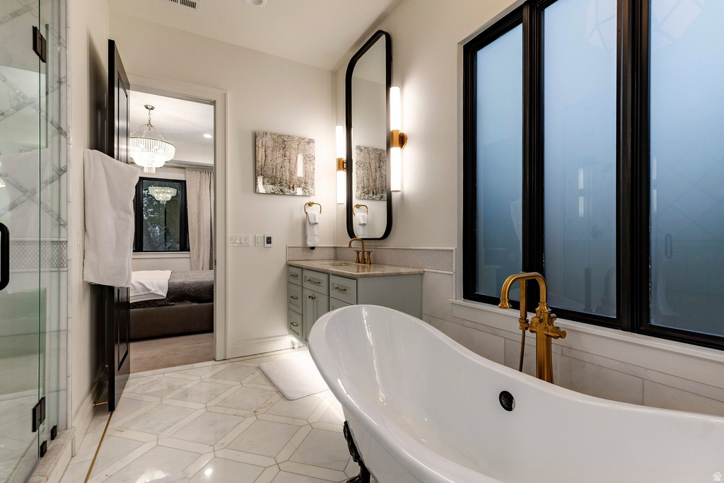 Freestanding soaking tub with brass fixtures, dual vanity with undermount sinks, geometric tile flooring, and a glass-enclosed shower