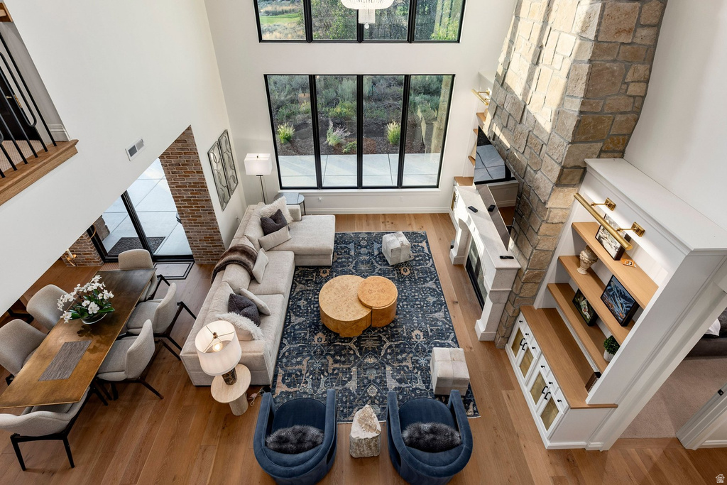 Double-height ceiling with expansive windows, stone fireplace, light wood-finish flooring, built-in shelving, and a formal dining area