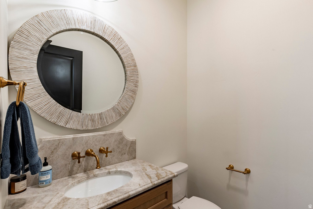 Neutral tone walls with an ornate round mirror, a vanity featuring a stone countertop, a built-in sink, and a wall-mounted brass faucet