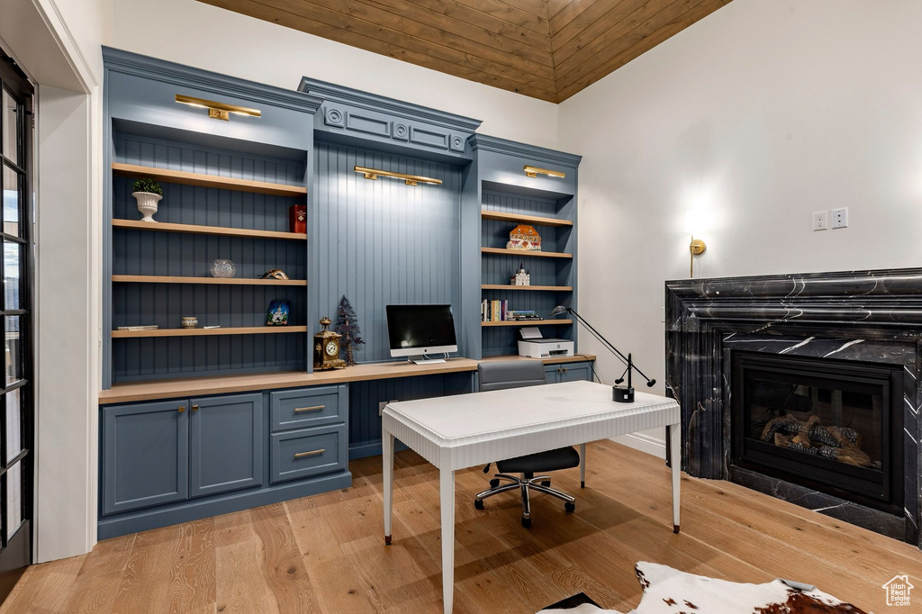 Built-in cabinetry with wood-finish shelving, wood-finish flooring, and a fireplace with a dark stone surround