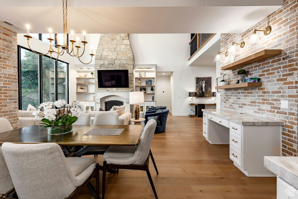 Hardwood flooring throughout, exposed brick accent walls, built-in desk with stone countertop, stone fireplace with built-in shelving, and a two-story ceiling