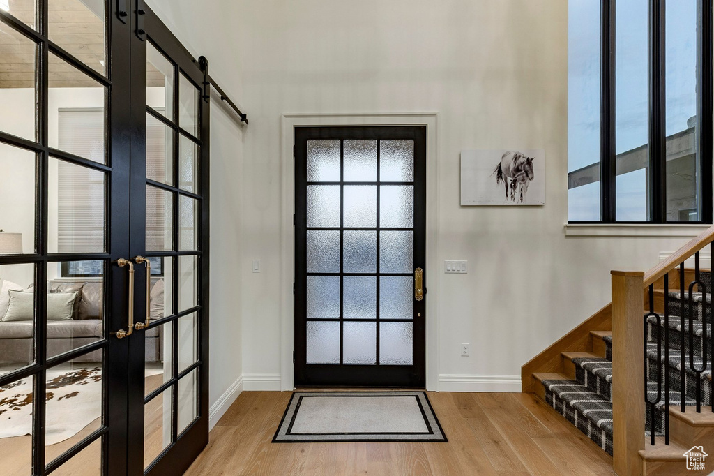 Entryway featuring wood-finish flooring, a black-framed door with frosted glass, a black-framed glass barn door, a wood staircase with black metal balusters, and a tall black-framed window