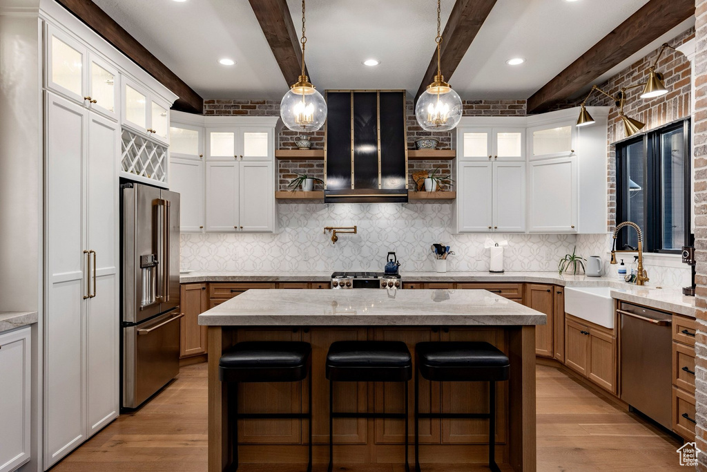 Gourmet kitchen featuring a central island with stone countertop, stainless steel appliances, wood-finish flooring, two-tone cabinetry, and exposed brick accents
