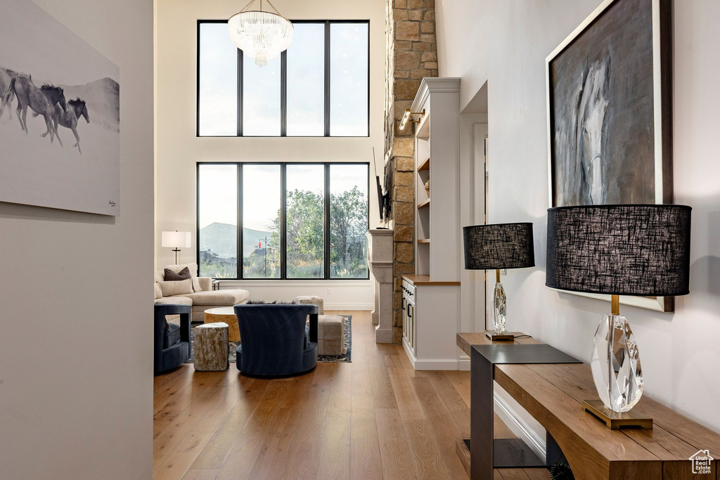 Double-height ceilings with expansive windows, a prominent stone-clad fireplace feature, built-in cabinetry, and wood-finish flooring