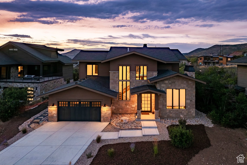 Contemporary exterior featuring stone veneer and wood siding, a multi-pane glass entry door, an attached two-car garage, and a concrete driveway