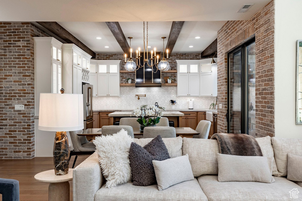Exposed brick accent walls, wood-finish flooring, white upper cabinetry, natural wood-finish lower cabinetry, and exposed ceiling beams