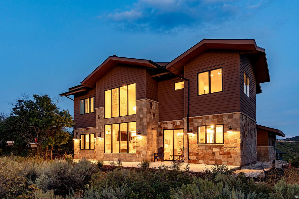 Multi-level exterior with board siding and stone accents, featuring large black-framed windows, a sliding glass door, and exterior sconce lighting