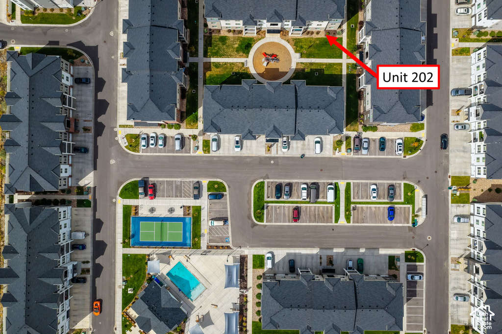 Community with multiple residential buildings, surface parking areas, a central landscaped courtyard, a tennis court, and a swimming pool