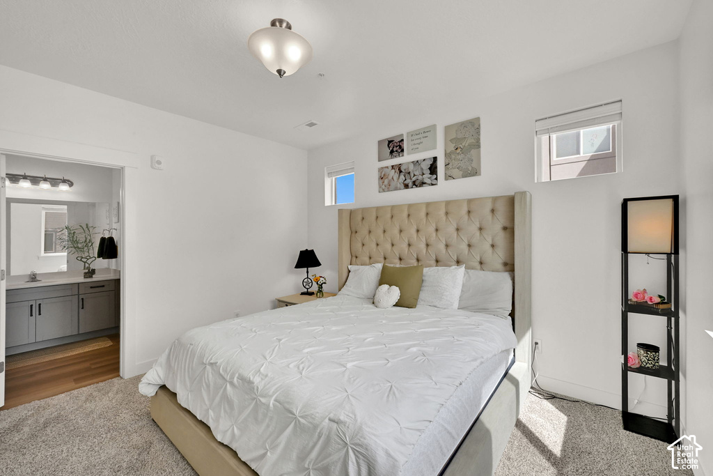 Tufted fabric headboard, recessed window, wall-mounted light fixture, vanity with dual-door cabinetry, and wood-finish flooring in the adjoining space