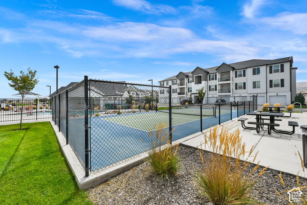 Hard court tennis court with chain-link fencing, adjacent recreational pool, and nearby outdoor dining area